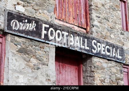 signe spécial de football de boisson peint à la main en bois fané sur le côté de l'entrepôt de mcdaids ramelton, comté de donegal, république d'irlande Banque D'Images