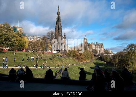 Visiteurs en silhouette par une belle journée d'automne assis dans East Princes Street Gardens admirant la vue sur le Scott Monument et l'hôtel Balmoral. Banque D'Images