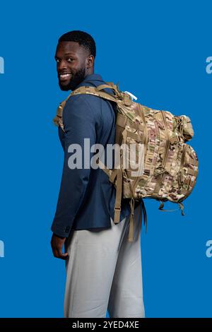homme noir avec sac à dos camouflage isolé sur fond bleu Banque D'Images