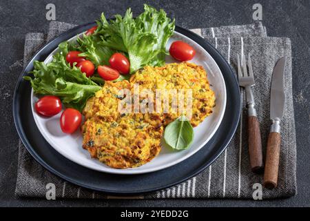 crêpes de pommes de terre à la carotte à la citrouille servies avec laitue et tomates fraîches sur assiette sur table en béton gris foncé avec couverts, serviette, vue horizontale, clos Banque D'Images