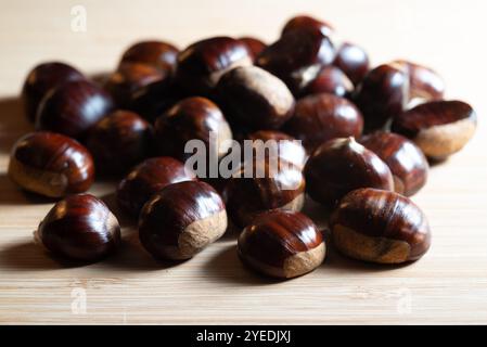 Image en gros plan montrant des coquilles de châtaignes crues disposées sur une table en bois, avec des textures d'automne brunes naturelles. Banque D'Images