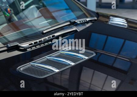 Gros plan des prises d'air chromées sur le capot d'une voiture noire, mettant en valeur un mélange de style et de performance qui rehausse l'agressivité A. Banque D'Images