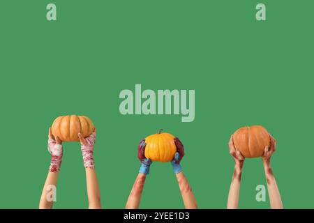 Mains de zombies avec des citrouilles mûres sur fond vert. Célébration d'Halloween Banque D'Images