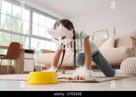 Quadrober fille dans le masque de chat avec bol d'alimentation à la maison Banque D'Images