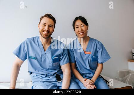 Portrait de professionnels de la santé masculins et féminins portant des gommages bleus et assis devant un mur Banque D'Images