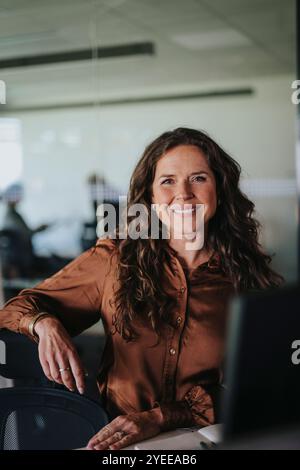 Portrait de femme d'affaires souriante avec de longs cheveux bruns assis dans le bureau Banque D'Images