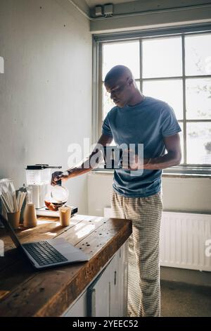 Entrepreneur masculin versant du café dans une tasse de papier tout en se tenant près de la table à l'atelier Banque D'Images