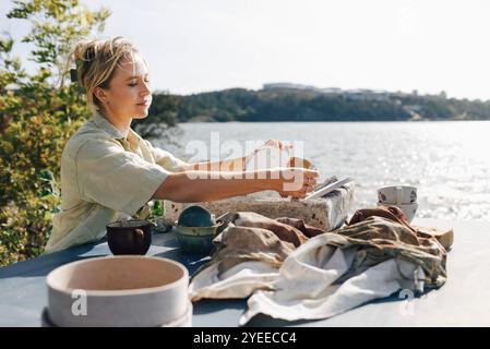 Femme artisan séchant des tasses en céramique sur table à la lumière du soleil Banque D'Images