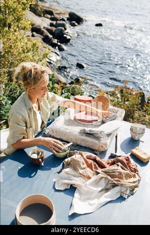 Vue à angle élevé femme artisan séchant des tasses en céramique sur la table à la lumière du soleil Banque D'Images