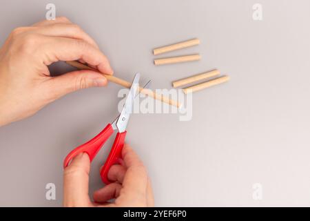 Un gros plan d'une main tenant une paire de ciseaux coupant la paille de papier, étape dans le processus créatif, bricolage, assemblage rapide, simplifié, jouet pour enfants, Banque D'Images