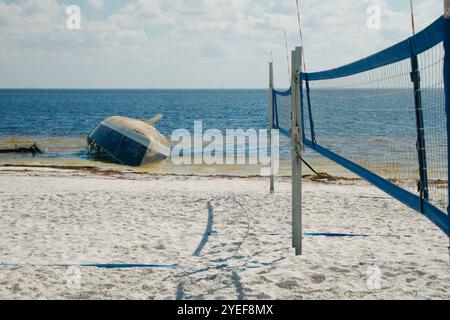 Filet de volley-ball de bord d'attaque large sur la droite avec vue sur une plage de sable blanc avec un voilier abandonné échoué retourné. Attention à Banque D'Images