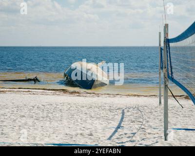 Filet de volley-ball de bord d'attaque large sur la droite avec vue sur une plage de sable blanc avec un voilier abandonné échoué retourné. Attention à Banque D'Images