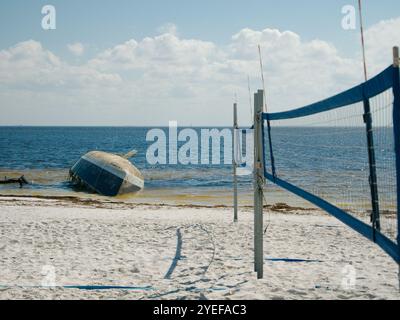 Filet de volley-ball de bord d'attaque large sur la droite avec vue sur une plage de sable blanc avec un voilier abandonné échoué retourné. Attention à Banque D'Images