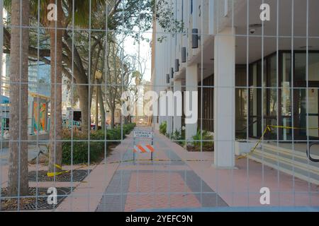 Vue à travers la clôture métallique jusqu'au trottoir en briques avec un panneau fermé orange et blanc en a-frame. Arbres sur les lignes d'attaque de gauche en bas de la rue vers Banque D'Images