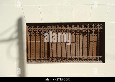 Vieux fer forgé isolé rouillé brun près du côté d'un mur de bloc ensoleillé clair. Ombre du poteau téléphonique et des fils à gauche. Vue large n° p Banque D'Images