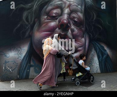 Femmes musulmanes marchant près d'une belle murale sur le mur Graffiti sur Carrer Nou de la Rambla à Barcelone, Espagne. Banque D'Images