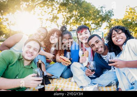 Groupe de personnes diverses s'amusant à la fête de jardin. Des amis heureux mangent de la nourriture et boivent du vin en pique-nique ensemble Banque D'Images