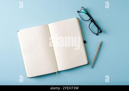 Vue de dessus du cahier, des lunettes et du stylo à bille sur fond bleu Banque D'Images