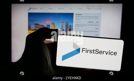 Personne tenant un téléphone portable avec le logo de la société canadienne FirstService Corporation sur l'écran devant la page Web. Concentrez-vous sur l'affichage du téléphone. Banque D'Images