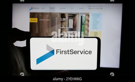 Personne tenant le téléphone cellulaire avec le logo de la société canadienne FirstService Corporation sur l'écran devant la page Web de l'entreprise. Concentrez-vous sur l'affichage du téléphone. Banque D'Images