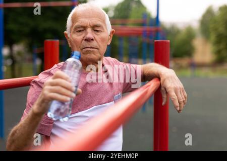 Homme âgé avec une bouteille d'eau se tenant entre des barres parallèles à l'extérieur Banque D'Images