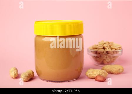 Beurre d'arachide savoureux en pot sur fond rose. Vue de dessus Banque D'Images
