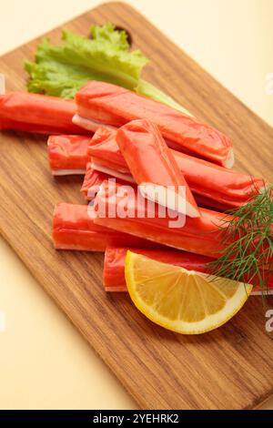 Bâtonnets de crabe frais avec citron sur planche à découper sur fond beige. Vue de dessus Banque D'Images