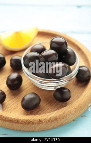 Olives noires avec citron sur plaque en bois sur fond bleu. Vue de dessus Banque D'Images