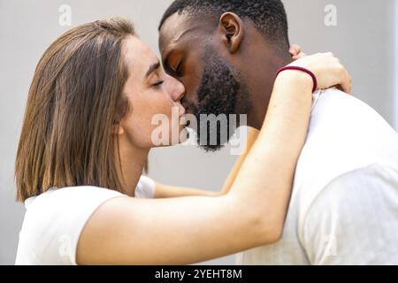 Vue de côté gros plan d'un couple multiracial d'amants habillé en blanc embrassant tendrement et embrassant Banque D'Images