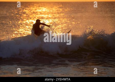 Une silhouette d'un surfeur chevauchant une vague lors d'un coucher de soleil magnifique. Banque D'Images