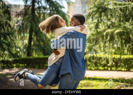 Femme caucasienne sautant pour embrasser son partenaire masculin africain dans un parc Banque D'Images