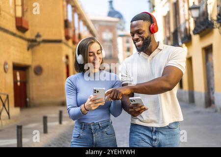 Heureux couple multi-ethnique écoutant de la musique et utilisant le téléphone portable marchant dans la ville Banque D'Images