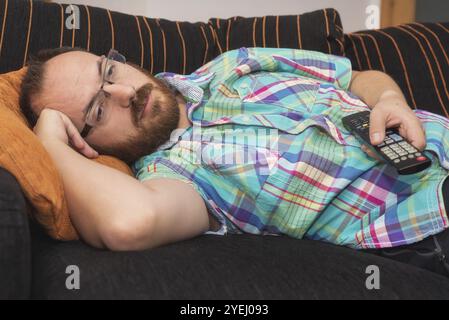 Homme se relaxant dans le canapé avec télécommande regardant la télévision Banque D'Images