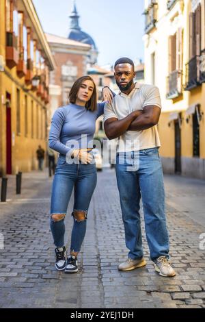 Portrait vertical sur toute la longueur d'un couple urbain multi-ethnique portant des vêtements en denim debout dans la rue Banque D'Images