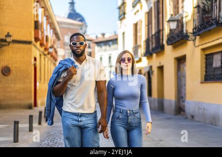 Vue frontale d'un couple multiracial élégant marchant ensemble avec attitude cool le long de la rue Banque D'Images