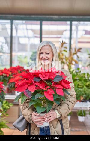 Une femme tient une plante en pot avec des fleurs rouges. Elle sourit et elle est heureuse Banque D'Images
