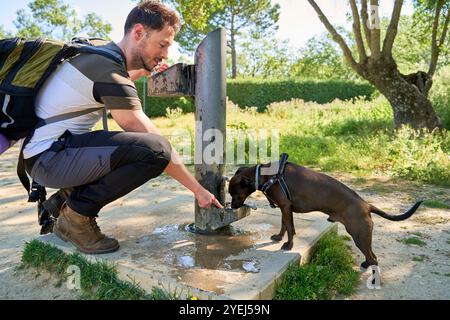 homme avec son chien buvant de l'eau de la fontaine de rue. Banque D'Images