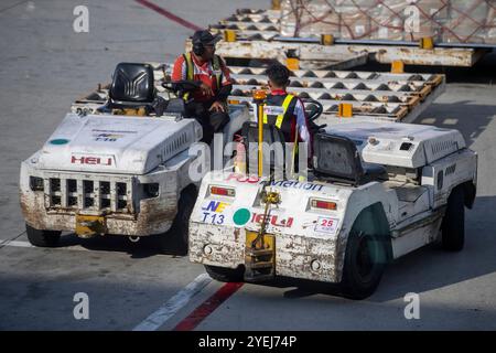 Deux membres de l'équipe au sol conduisent des véhicules de remorquage de bagages à l'aéroport, communiquant tout en travaillant sur le transport de marchandises à l'aéroport. Banque D'Images