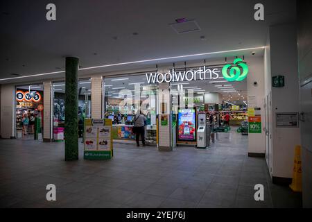 Vue rapprochée de l'entrée d'un magasin Woolworths, montrant la signalisation lumineuse Woolworths, les caisses libre-service et les affichages publicitaires. Banque D'Images