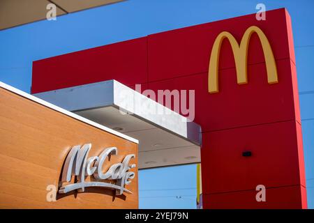 Enseigne McDonald's avec arcs dorés et logo McCafé, mettant en valeur l'emblématique marque de restauration rapide sur un rouge vif et une texture bois. Banque D'Images