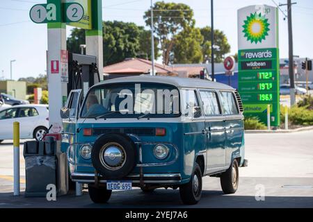 Une fourgonnette Volkswagen Kombi bleue vintage se ravitaillant dans une station-service BP, présentant un véhicule classique à la pompe avec des panneaux de prix de l'essence en arrière-plan. Banque D'Images