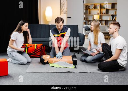 Jeune homme instructeur aidant à faire des compressions cardiaques de premiers soins avec mannequin pendant l'entraînement de groupe à l'intérieur. Banque D'Images