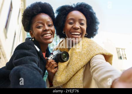 Deux amis heureux prenant un Selfie joyeux dans la ville tout en tenant un appareil photo, embrassant l'amitié et l'aventure urbaine Banque D'Images