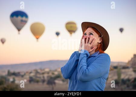 Dans la lumière tôt le matin, un voyageur ravi regarde avec admiration les montgolfières colorées s'élever au-dessus du paysage unique de la Cappadoce créant une magie Banque D'Images