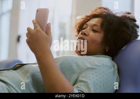 Femme allongée sur le canapé et utilisant des applications pour smartphone pour le divertissement et la communication tout en se relaxant dans un environnement confortable à la maison par jour lumineux Banque D'Images