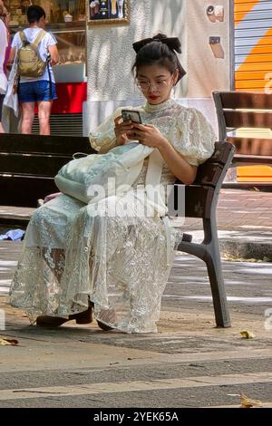 Une femme asiatique portant une robe blanche assise sur un banc à Avinguda de Gaudí à Barcelone, Espagne. Banque D'Images