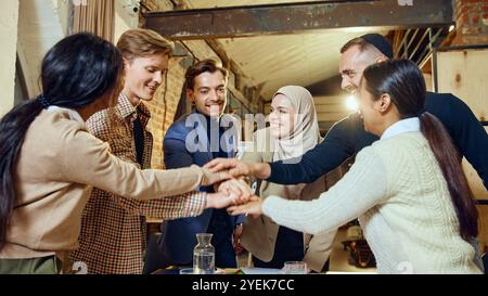 Une équipe multiculturelle dans un cadre de bureau ouvert et détendu célèbre l'unité en mettant les mains ensemble. Banque D'Images