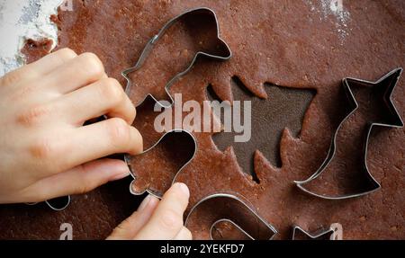 Mains de garçon coupant différentes formes de pâte à pain d'épices roulée avec des coupe-fils en métal de Noël avec des motifs tchèques traditionnels. Le processus de fabrication Banque D'Images