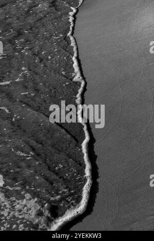 Vagues matinales sur Sandy Beach : contraste de surface humide et sèche sur le littoral. Noir et blanc. Grèce 2024 Banque D'Images