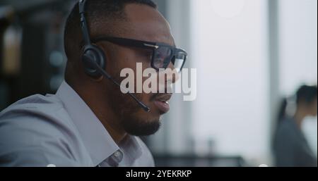 Gros plan de l'opérateur de hotline afro-américaine dans le casque ayant conversation sur appel avec le client, fournissant une assistance en ligne pour le client. Le spécialiste du support technique travaille dans le bureau du centre d'appels. Banque D'Images